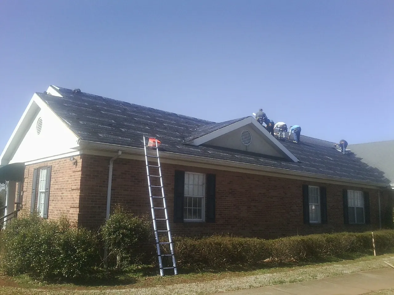 Crew tearing shingles off a brick ranch roof with a ladder set — Metal Roof Repair work by our crew in Wilton