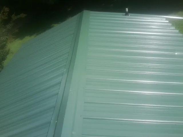 New green metal panels meeting at the ridge of a roof — Flat Roof Repair work by our crew in Wilton
